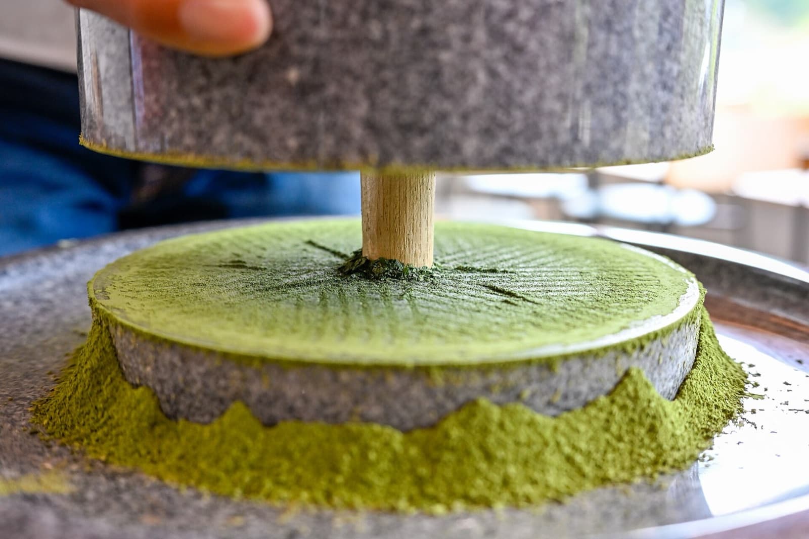 Pale green matcha powder falling from a stone mill