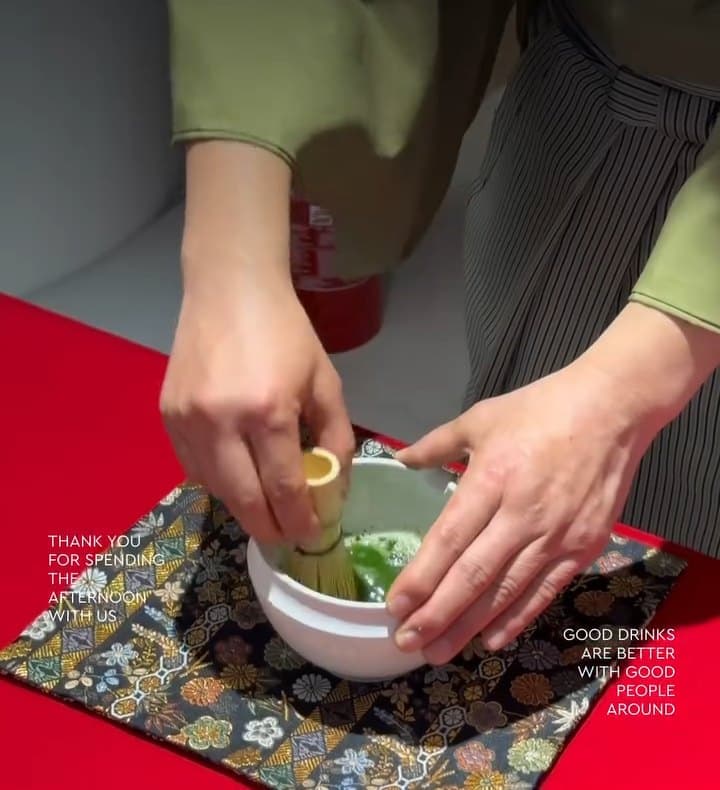 Hands whisking matcha in a white bowl on red cloth and brocade