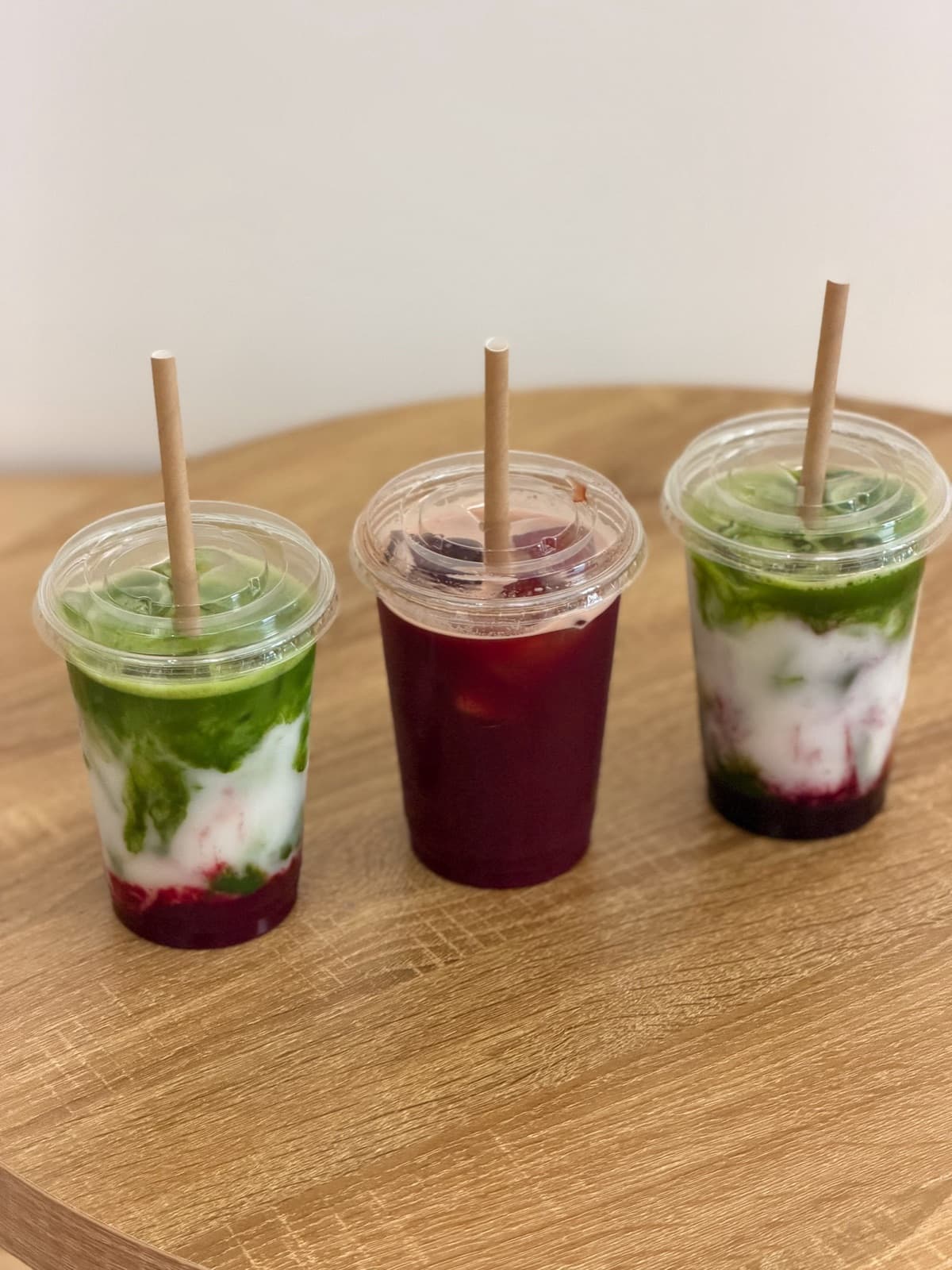 Three layered matcha drinks with straws on a wooden table at MatchaBa